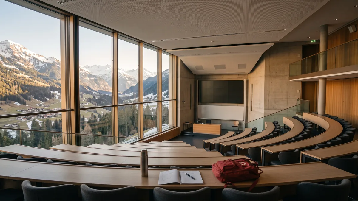 Amphithéâtre universitaire avec vue sur les Alpes, cahier et sac posés sur un pupitre